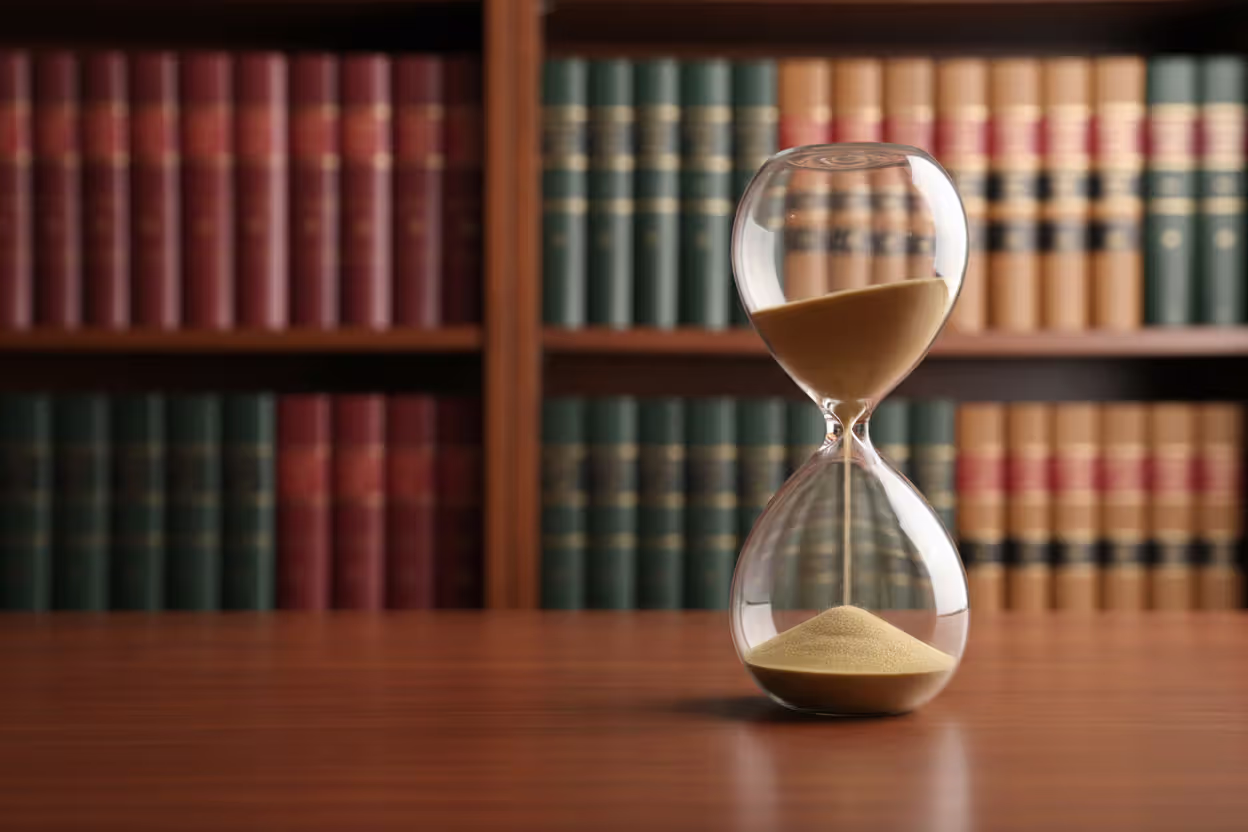 Hourglass on a polished wooden desk with blurred law books on shelves in the background symbolizing timely planning