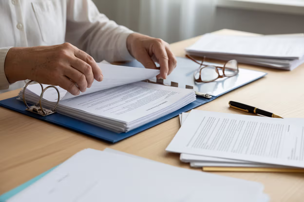 Close-up of elderly person's hands organizing important documents into a neat folder on a tidy desk
