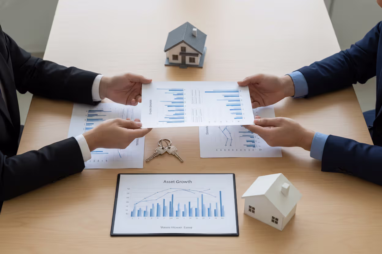 Top view of a business table with estate documents, asset growth charts, house keys, and a small house model with two people exchanging papers
